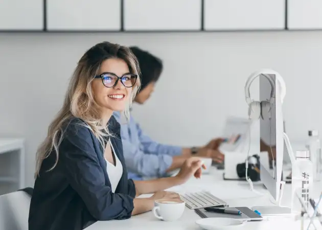 Mulher em frente a um computador olhando para a câmera e sorrindo